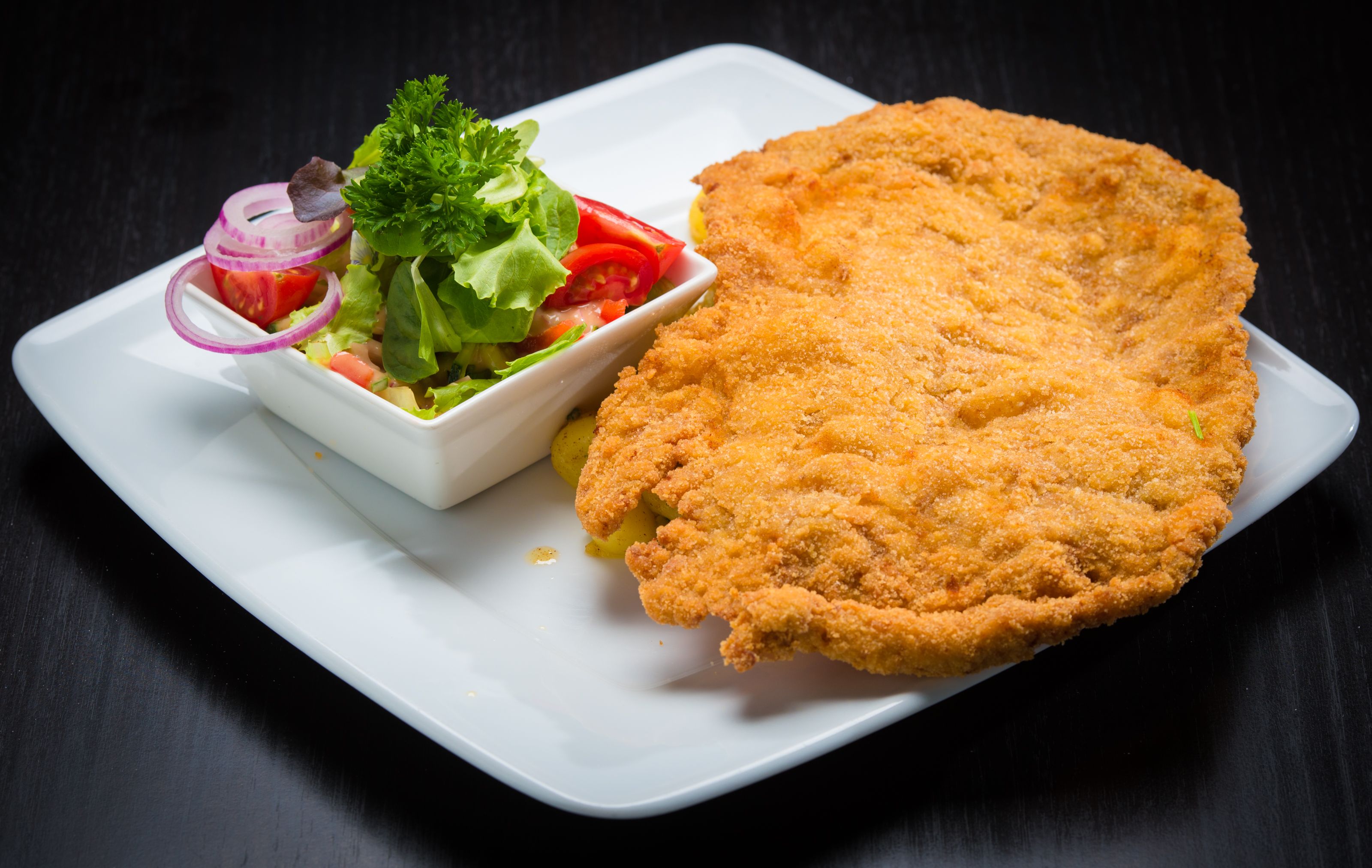A golden cotoletta alla milanese on a white plate with a lemon wedge